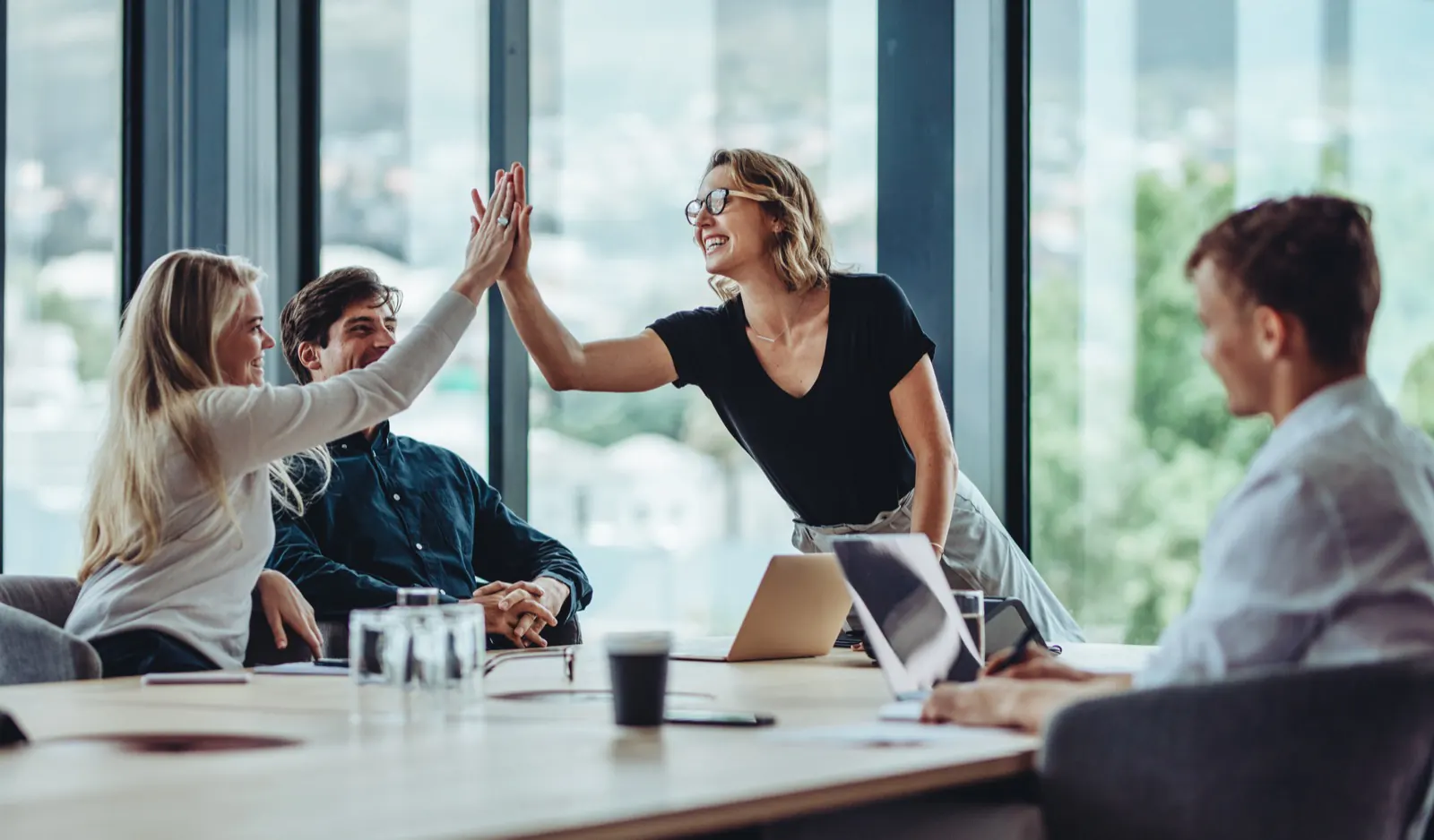 Ett team ger varandra high-five runt ett mötesbord efter ett lyckat samarbete
